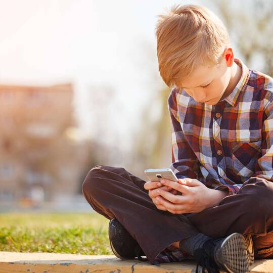 ein Junge sitzt draußen auf dem Boden mit seinem Smartphone