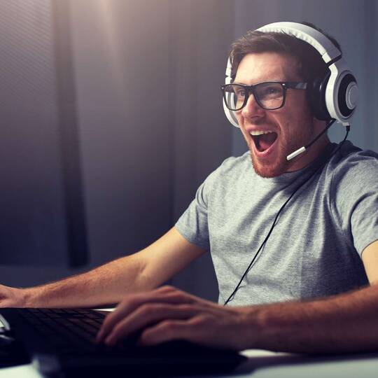 Mann mit Headset sitzt freudig vor Gaming Laptop