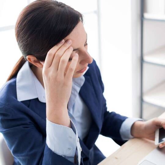 Eine Frau sitzt an einem Schreibtisch und hat ihr Smartphone in der Hand