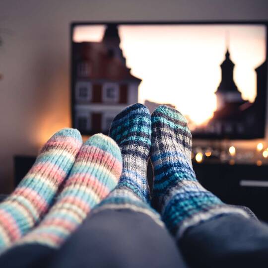 Zwei Paar Füße in Stricksocken vor Fernseher
