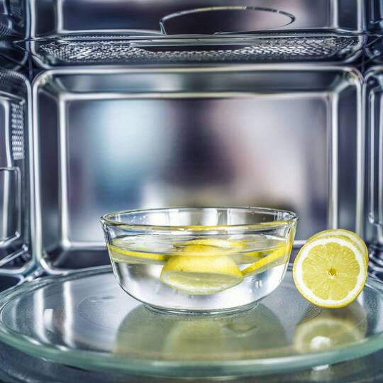 Eine Schale mit Wasser, Essig und aufgeschnittenen Zitronen steht in einer Mikrowelle