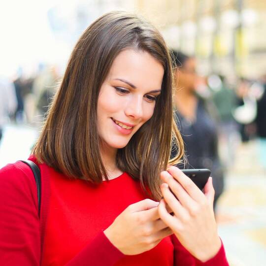 Frau in rotem Pullover schaut auf ihr Smartphone