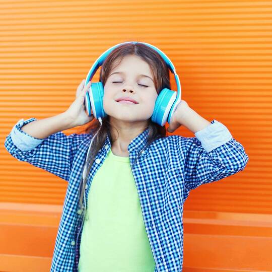 Kind mit blauen Kopfhörern vor gelbem Hintergrund freut sich