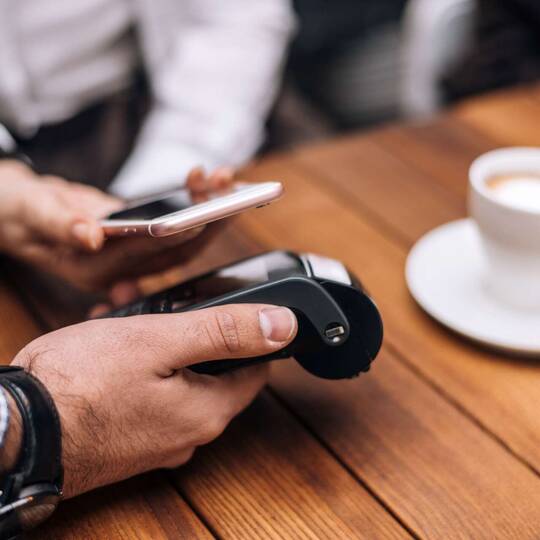 Frau bezahlt am Tisch in einem Café ihren Kaffee mit ihrem iPhone
