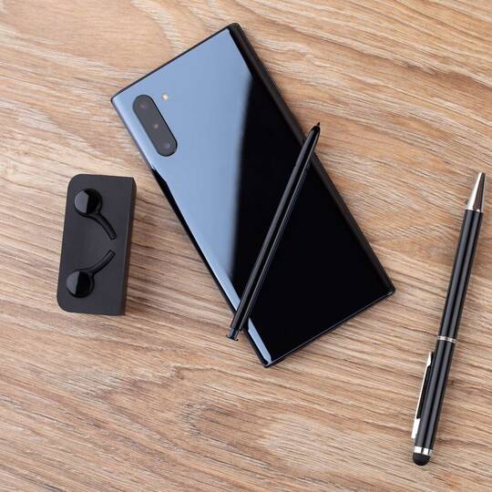 Samsung Galaxy Note 10 liegt neben Bluetooth-Kopfhörern und Stift mit der Rückseite nach oben auf einem Holztisch