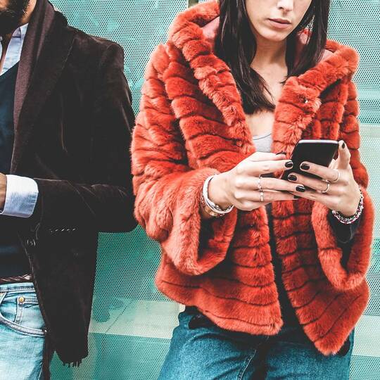 Mann und Frau in Designer-Klamotten bedienen ihr ihr Smartphone