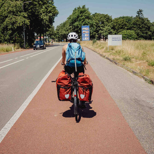 Frau fährt auf Fahrrad mit Gepäcktaschen über den Radweg.