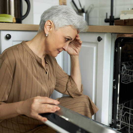 Frau sitzt verzweifelt vor ihrer Spülmaschine