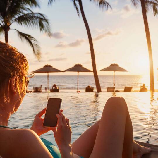 Frau liegt mit Smartphone an einem Swimmingpool