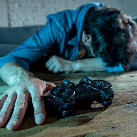 Mann liegt verzweifelt am Boden mit Hand am Controller