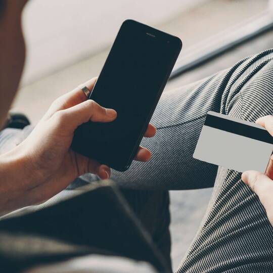 Ein Mann hält neben seinem Smartphone eine Kreditkarte in der Hand