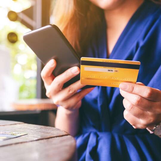 Frau tippt Kreditkarten-Daten in Smartphone ein