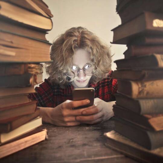 eine Person schaut auf ihr Smartphone. Rechts und links stehen Bücher