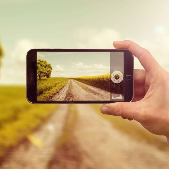 Person fotografiert einen Feldweg mit dem Smartphone
