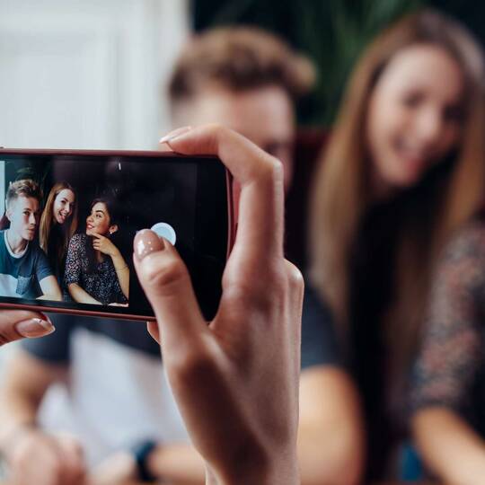 Person macht ein Foto von drei Jugendlichen mit dem Smartphone