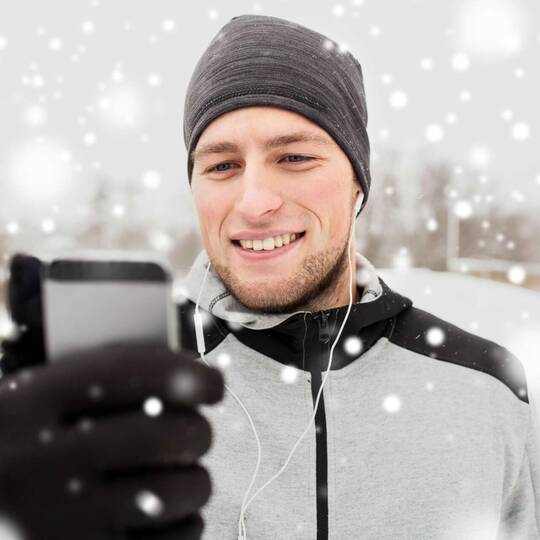 Mann hält Handy, während es schneit
