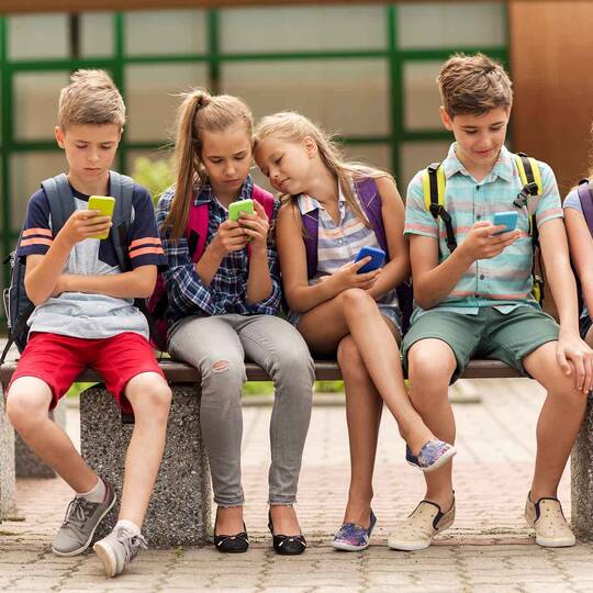 Schulkinder sitzen auf Bank und schauen auf ihre Smartphones