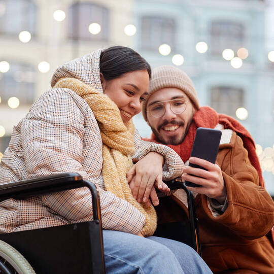 Frau im Rollstuhl und Mann machen im Winter ein Selfie