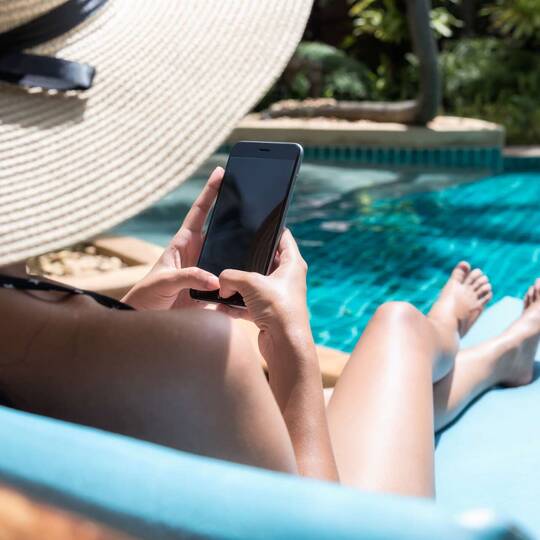 Frau liegt mit Smartphone am Pool
