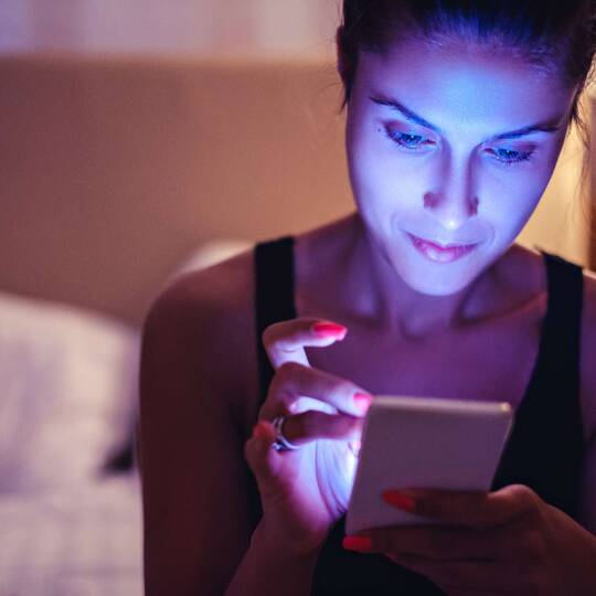 Junge Frau sitzt auf dem Bett und tippt am Smartphone