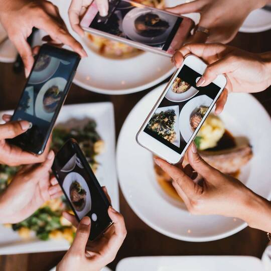 Vier Personen machen Fotos von ihrem Essen mit ihren Smartphones
