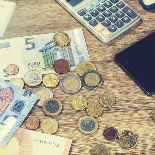 Bargeld, Taschenrechner und Smartphone liegen auf Tisch 