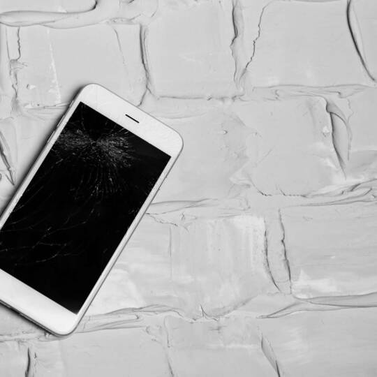 iPhone liegt mit gesplittertem Display auf grob gespachtelten Untergrund