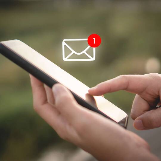 Person bedient Smartphone, über welchem ein Briefsymbol zusehen ist, welches eine neue Nachricht indiziert