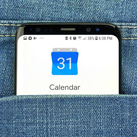 Smartphone mit Google Kalender Applikation ragt aus Jeans-Hosentasche