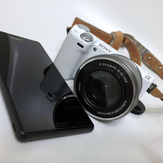 Ein schwarzes sony Smartphone und eine weiße Kamera auf einem weißen Hintergrund.
