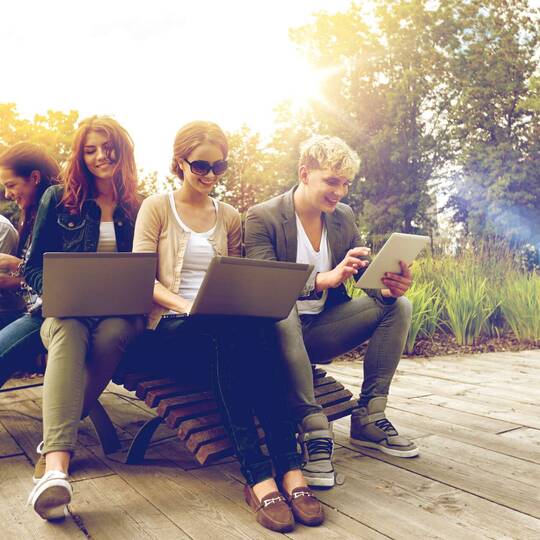 Eine Gruppe Studenten sitzt draußen an ihren Laptops und Tablets