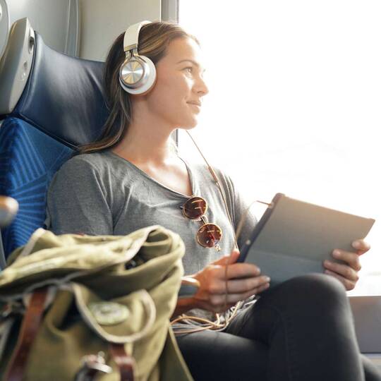 Frau sitzt mit Kopfhörern und Tablet im Zug 