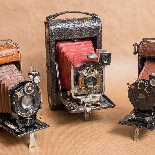 Drei Oldtimer Fotokameras auf einem beigen Hintergrund.