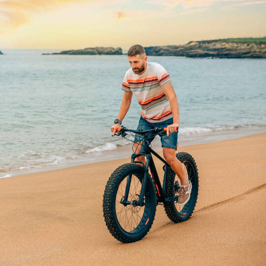 Mann fährt auf Fatbike Strand entlang.