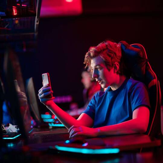 Mann sitzt in dunkler Umgebung an Gaming Laptop