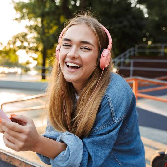 Jugendliche mit Kopfhörern und Smartphone in den Händen schaut lächelnd in die Kamera
