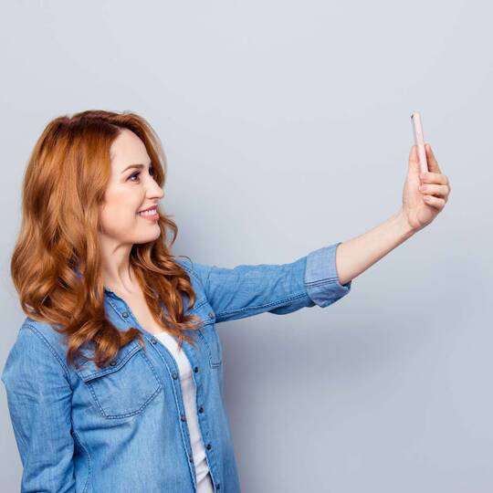 Eine Frau hält ein Smartphone in der Hand und macht ein Foto von sich selbst.