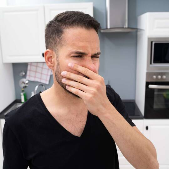 Mann steht mit Hand vor Mund und angewidertem Gesichtsausdruck vor Kühlschrank