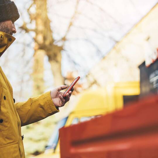 Mann mit Winterjacke und Mütze bedient Smartphone