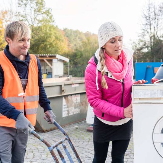 Zwei Personen stehen mit Waschmaschine und Sackkarre auf Wertstoffhof