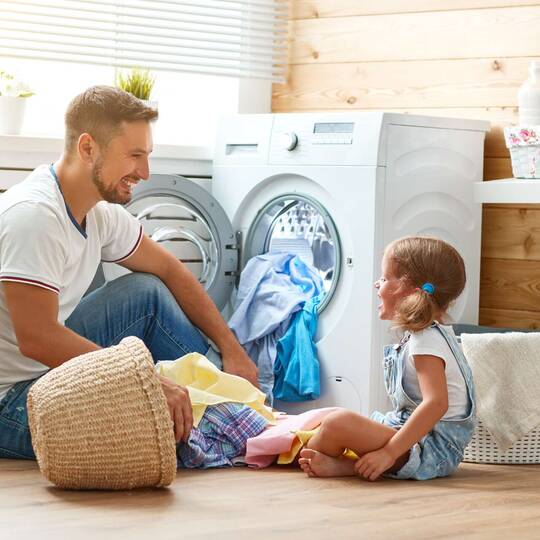 Mann und und Kinde sitzen mit Wäsche vor Waschmaschine