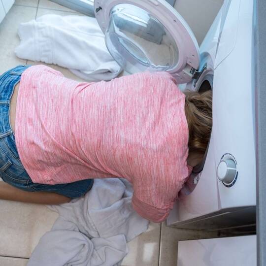Frau kniet vor einer Waschmaschine mit ihrem Kopf in der Trommel