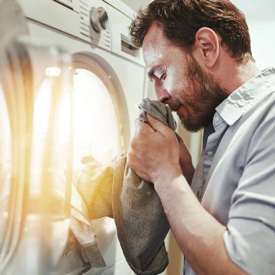 Mann riecht an der Wäsche aus der Waschmaschine