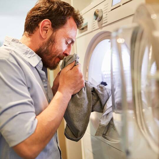 Mann riecht an Wäsche, die aus Maschine kommt