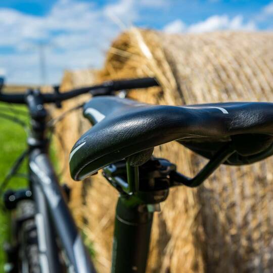 Foto eines Fahrrads, welches an einem Strohballen lehnt, mit Fokus auf den Fahrradsattel