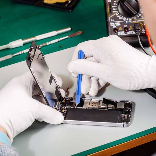 Zwei Hände in Handschuhen reparieren mit Werkzeug ein Smartphone