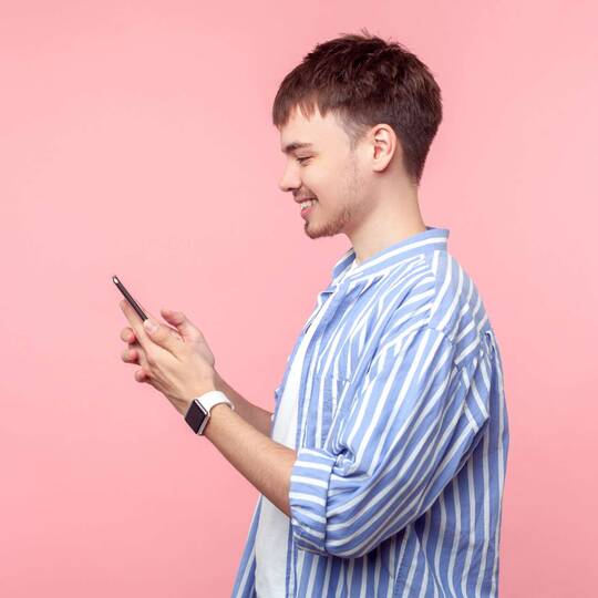 Mann steht vor einem pinken Hintergrund und lächelt auf sein Smartphone