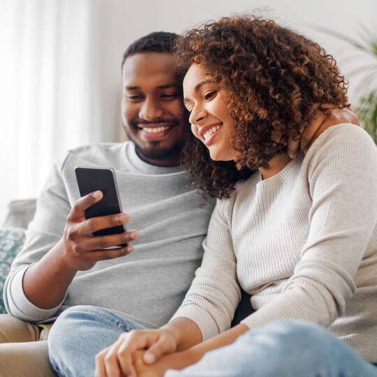 Zwei Personen auf einer Couch schauen lächelnd auf Smartphone